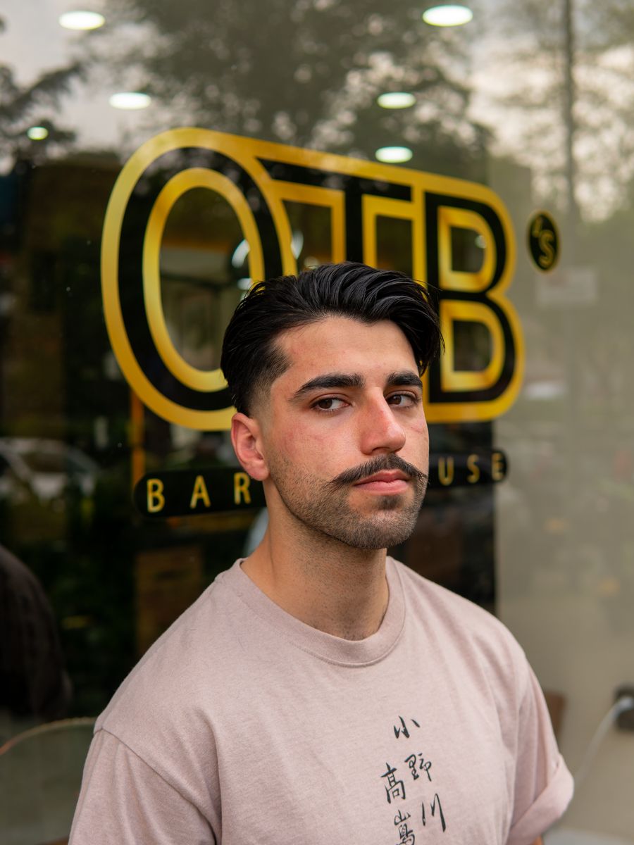 Slick back with moustache in front of the OTB's Barberhouse logo at OTB's Barberhouse